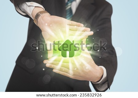 Hands creating a form with shining green house in the center