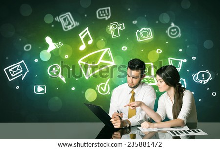 Business couple sitting at the black table with social media symbols on the background