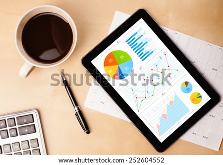 Workplace with tablet pc showing charts and a cup of coffee on a wooden work table close-up