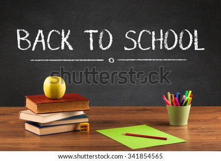 Back to school concept with writing on blackboard in capital letters and a desk with papers, fruit
