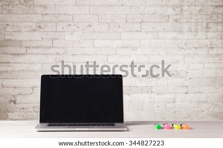 An open laptop on an office desk with flower, coffee, books in front of white brick wall background concept
