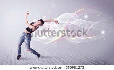 A beautiful young hip hop dancer dancing contemporary urban street dance in front of grey wall background with smokey lines and glitter concept.