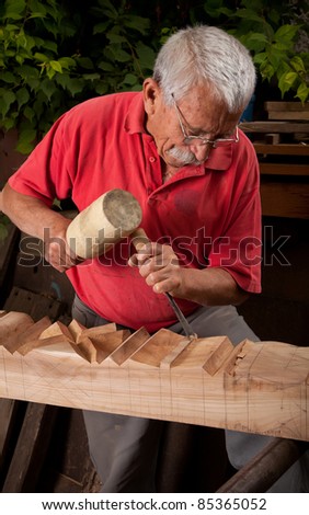Old woodcarver working with mallet and chisel