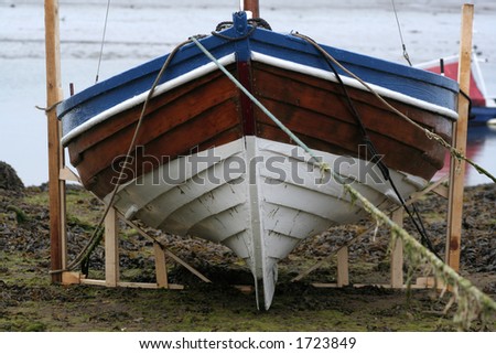 Boat is brought out of the water onto the shore and its owners hvae made a frame for it so that it can stay upright on the shore, otherwise without support it would just lie on its side