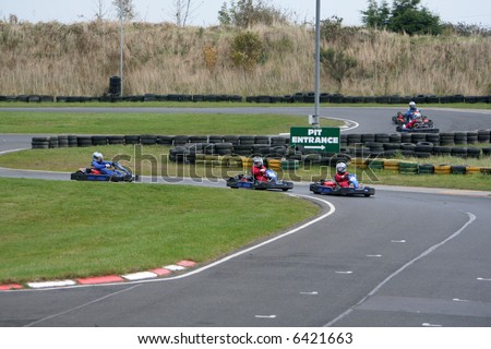 Go kart drivers race past the pit stop entrance and speed around the track