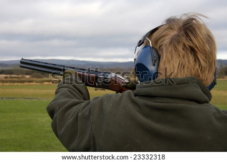 Teenage boy holds the gun to the left to fire a at the clay pigeon