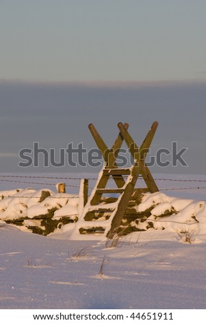 Wooden stile which enables walkers to get over the fence is covered in snow
