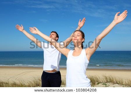 Couple meditating at the beach with arms up