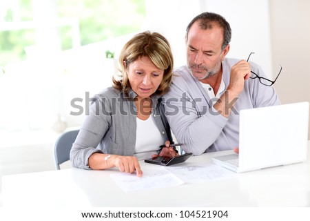 Couple reading construction plan at home with use of laptop