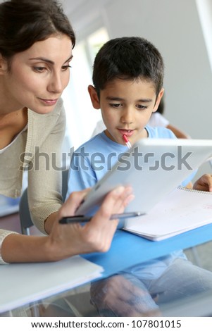 Teacher and schoolboy using electronic tablet in class