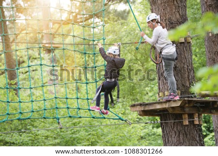 Little girl at adventure park climbing trees with secured ropes