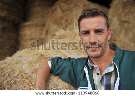 Portrait of cheerful farmer standing in front of hay rolls