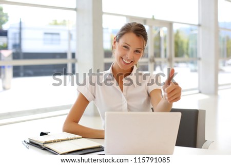 Cheerful office-worker showing thumbs up in front of laptop