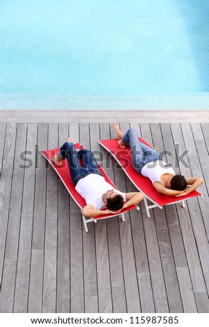Couple relaxing in long chairs by outdoor pool