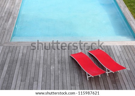 View of red long chairs set by swimming-pool