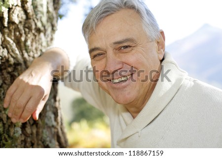 Portrait of smiling senior man leaning against tree