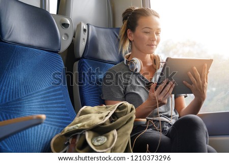 Young woman travelling by train with tablet and headphones