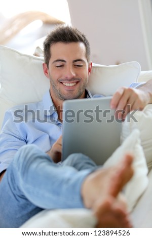 Cheerful young man laying in sofa with digital tablet