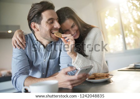Gorgeous fun couple feeding eachother cookies in modern kitchen