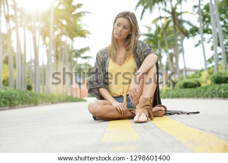 Bohemian woman sitting in middle of road surrounded by palm trees
