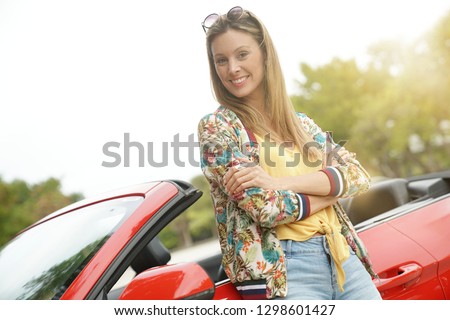 Attractive young woman leaning on red convertible car