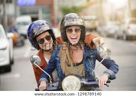 Happy young women riding scooter together in city