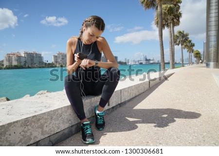 Smily sporty young woman checking cellphone in sunny outdoors