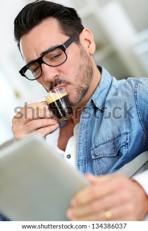 Man with glasses drinking coffee and using tablet