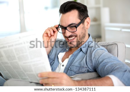 Cheerful guy reading newspaper in sofa