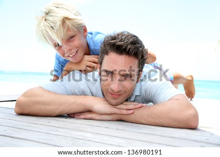 Young boy laying over his dad's back by pool