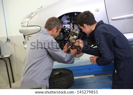 Instructor showing student how to change car brakes