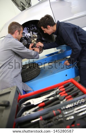 Instructor showing student how to change car brakes