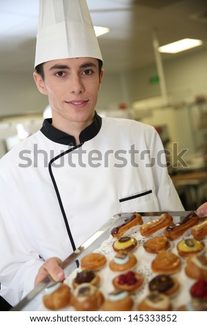 Young pastry cook holding tray of pastries
