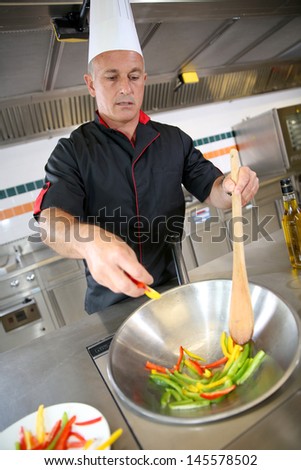 Chef in restaurant kitchen preparing wok of vegetables