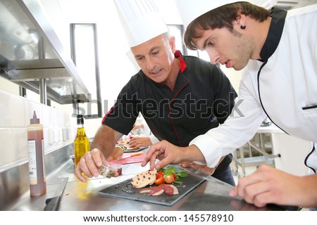 Chef helping student in catering to prepare foie gras dish
