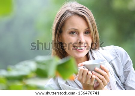 Beautiful smiling woman drinking hot drink in garden
