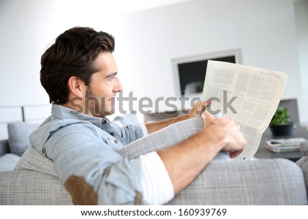 Handsome guy at home reading newspaper
