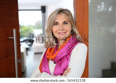 Cheerful senior woman standing at home entrance door