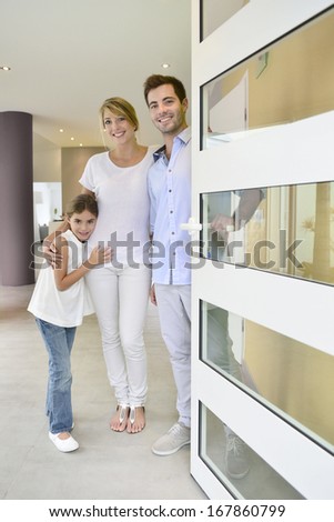 Family Standing At Front Door To Invite People In