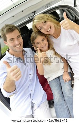 Cheerful family in car trunk showing thumbs up