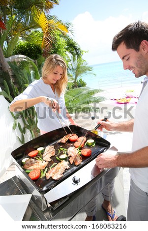 Cheerful couple preparing grilled food on barbecue