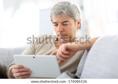 Mature man in sofa websurfing with tablet
