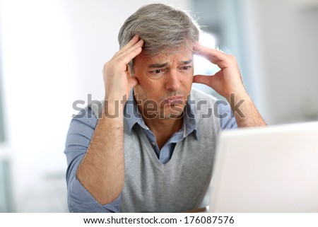 Senior businessman in front of laptop having a headache