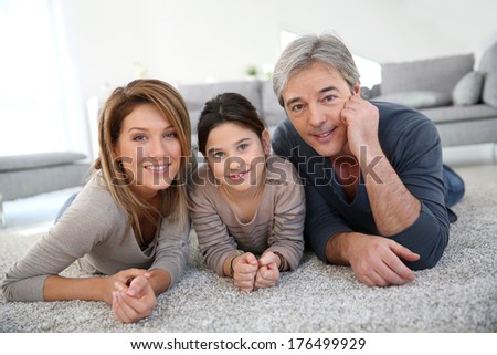 Middle-aged couple with little girl laying on carpet