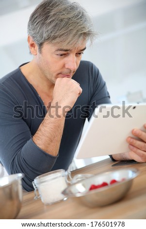 Man looking at recipe on digital tablet to prepare cake