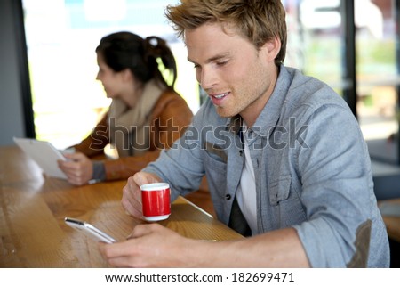 Young man in coffee shop wonnected on smartphone