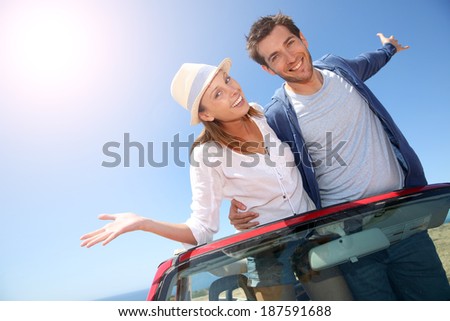 Funny couple with arms up from convertible car