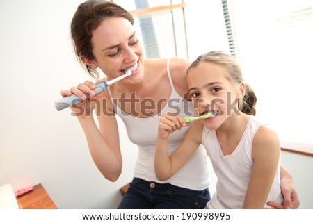 Mother teaching little girl how to brush her teeth