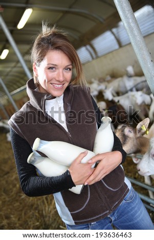 Smiling farmer holding bottles of goat milk in barn