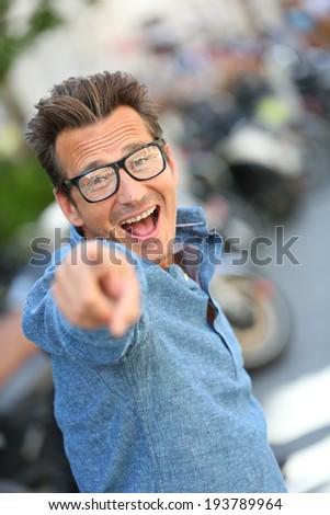 Cheerful guy with eyeglasses pointing at camera